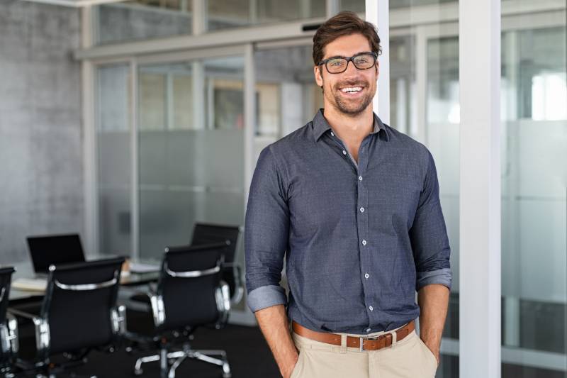 Man Standing In His Office Smiling After Speaking With A Whole Life Insurance Advisor