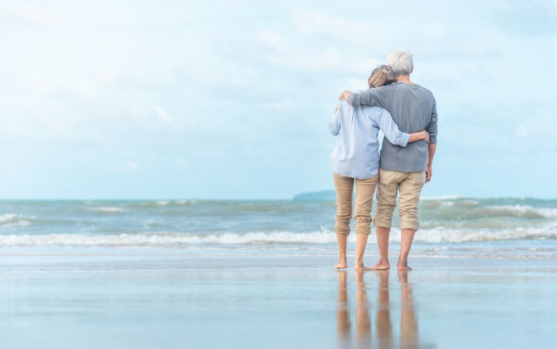Man & Woman Walking Along The Beach After Their Life Insurance Settlement